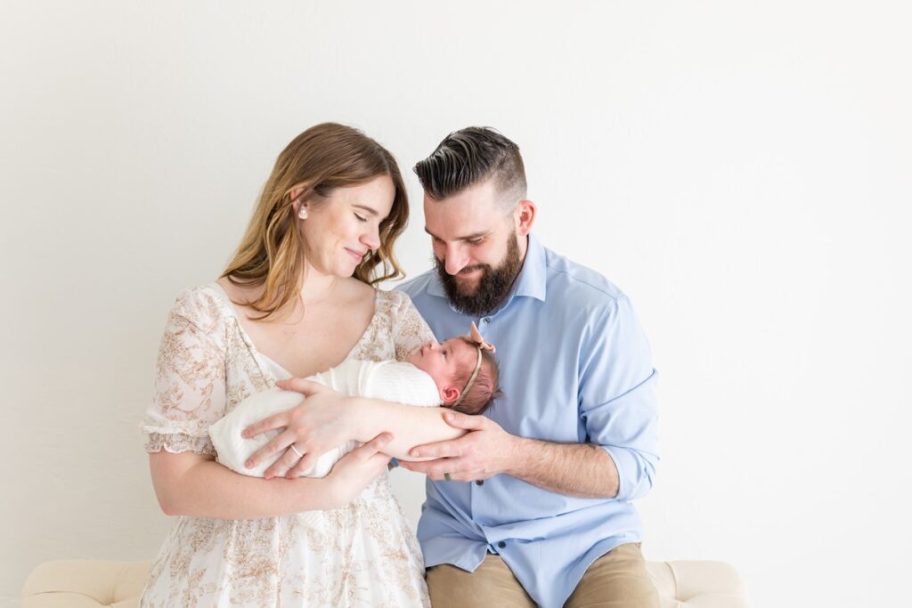 Mom and Dad sitting holding newborn baby girl swaddled 