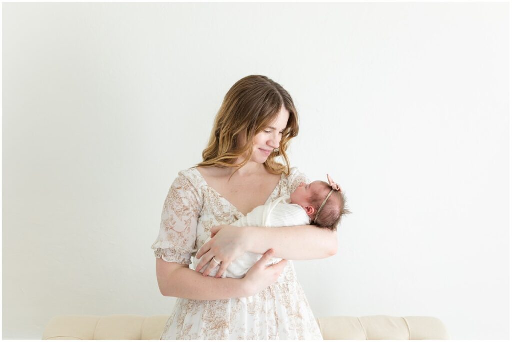 Mom sitting holding newborn baby girl swaddled 