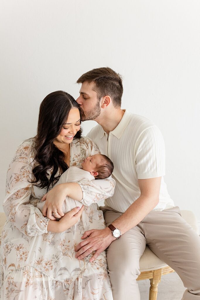 mother and father sitting in okc newborn photographer studio holding swaddled newborn