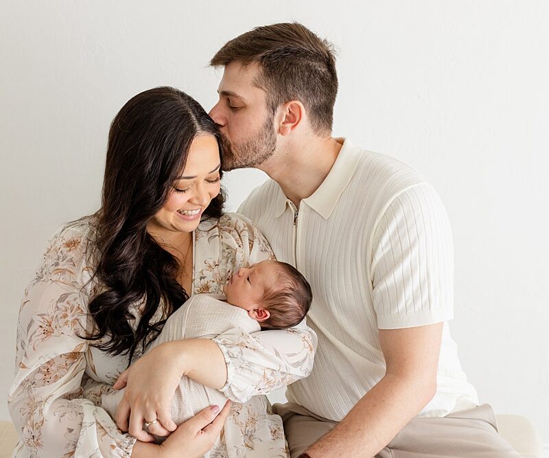 mother and father siiting in okc newborn photographer studio holding swaddled newborn