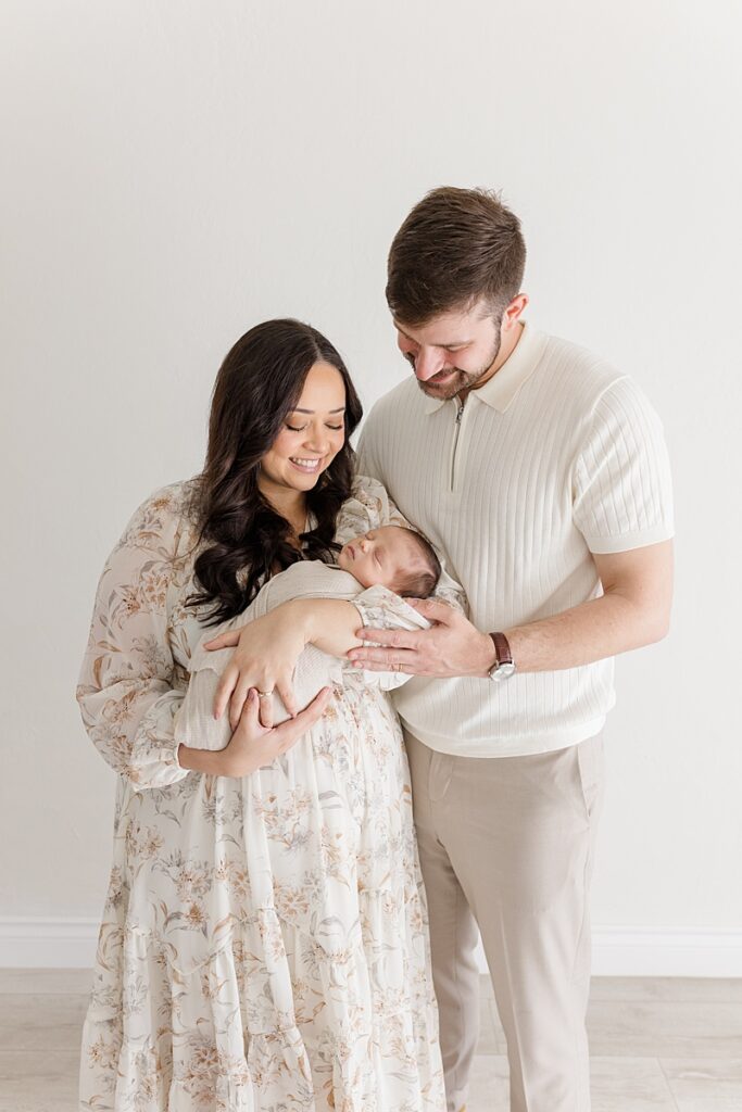 mother and father standing holding swaddled newborn in okc newborn photographer studio